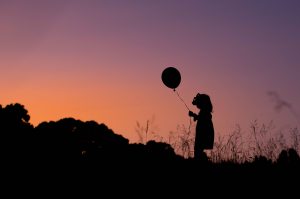 Girl with bow holding balloon at sunset