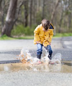 Boy with yellow raincoat jumping in puddle
