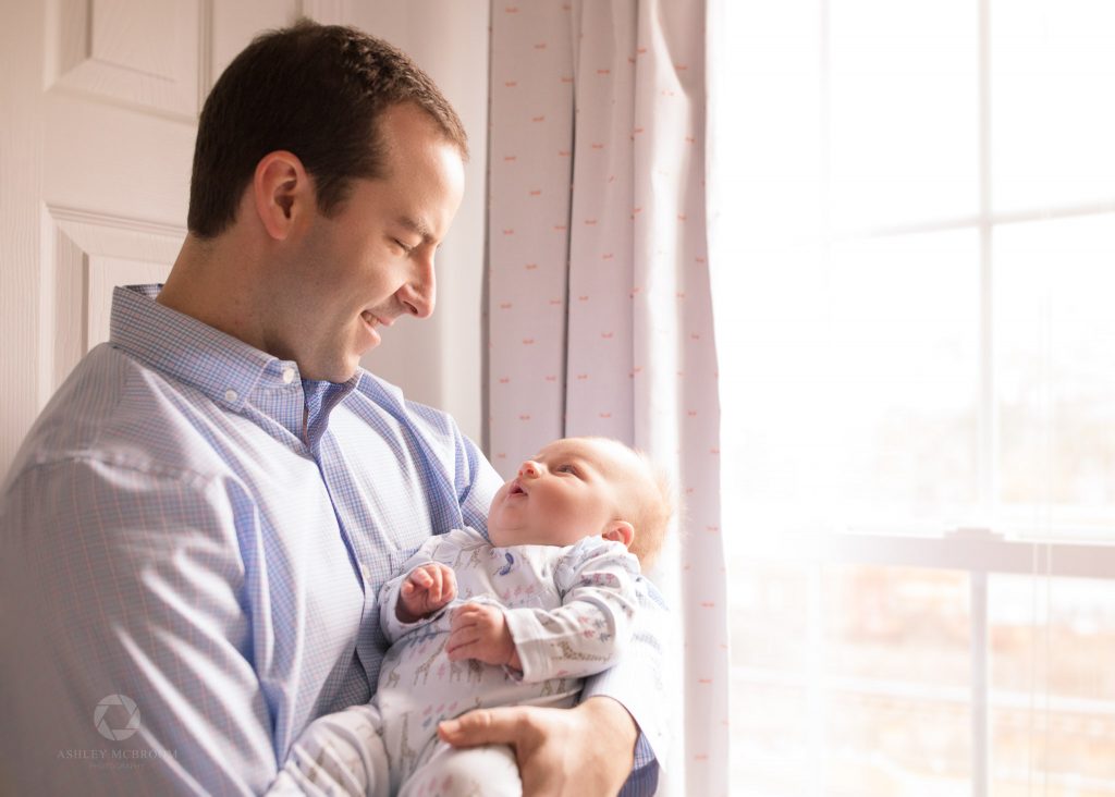 Dad holding baby who is looking up at him by window
