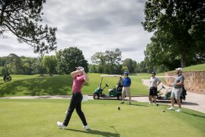 man hitting golf ball while teammates look on