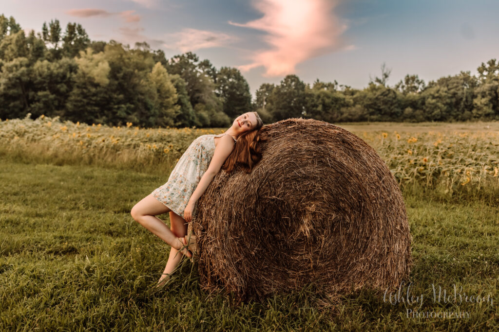 High school senior amidst sunflowers leaning on a hay bale