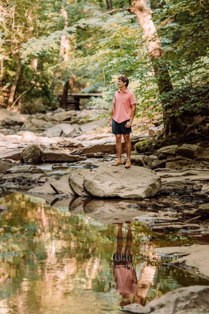 Walton high school senior standing on a rock by a creek with his reflection in the water during senior photos in Marietta GA