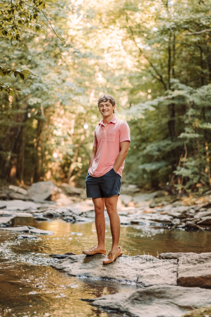 relaxed senior guy in polo shirt balancing on the rocks amidst a beautiful creek during golden hour