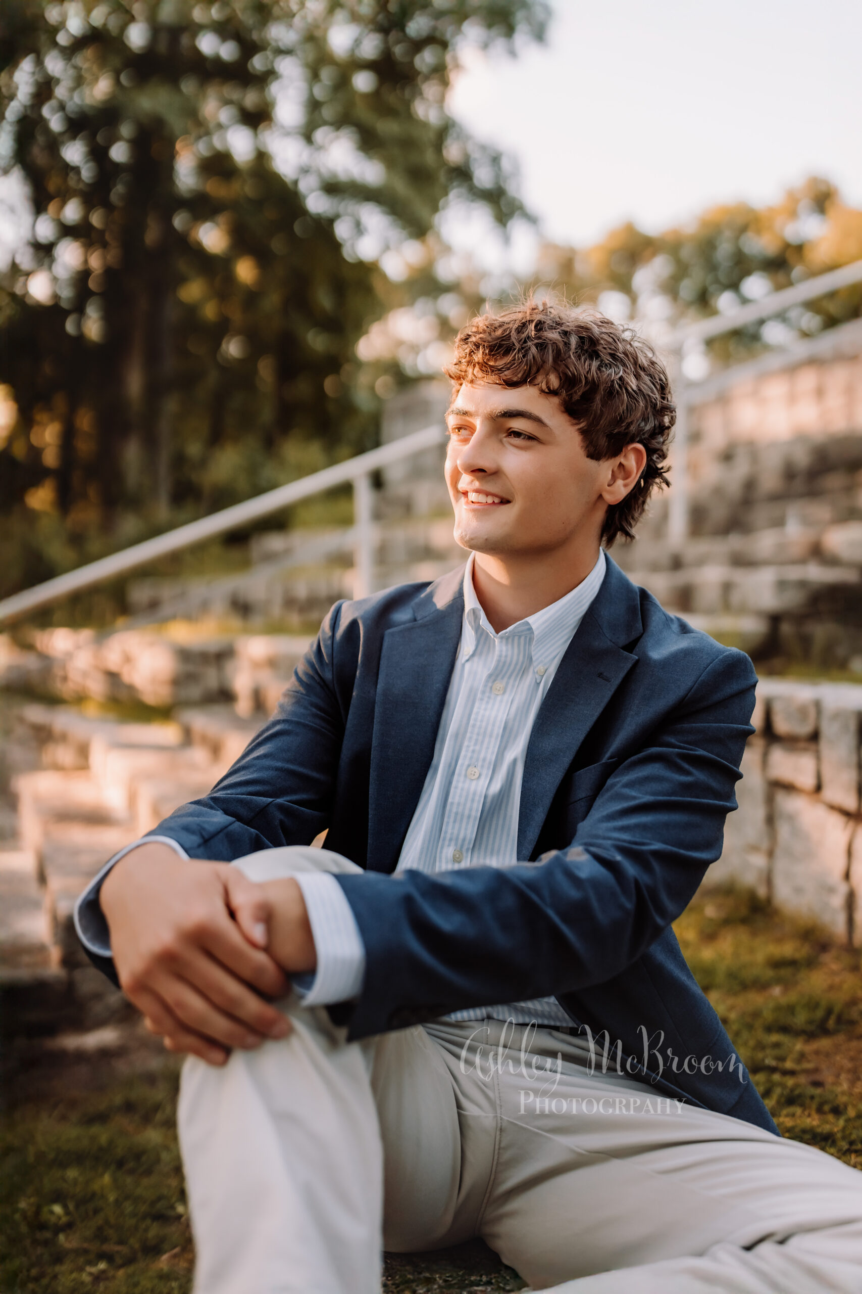 High school senior boy in blue blazer looking off into sunset on stone steps