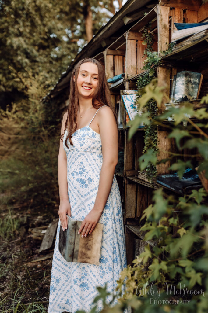 Campbell high school IB program senior holding a book in front of a rustic outdoor bookshelf