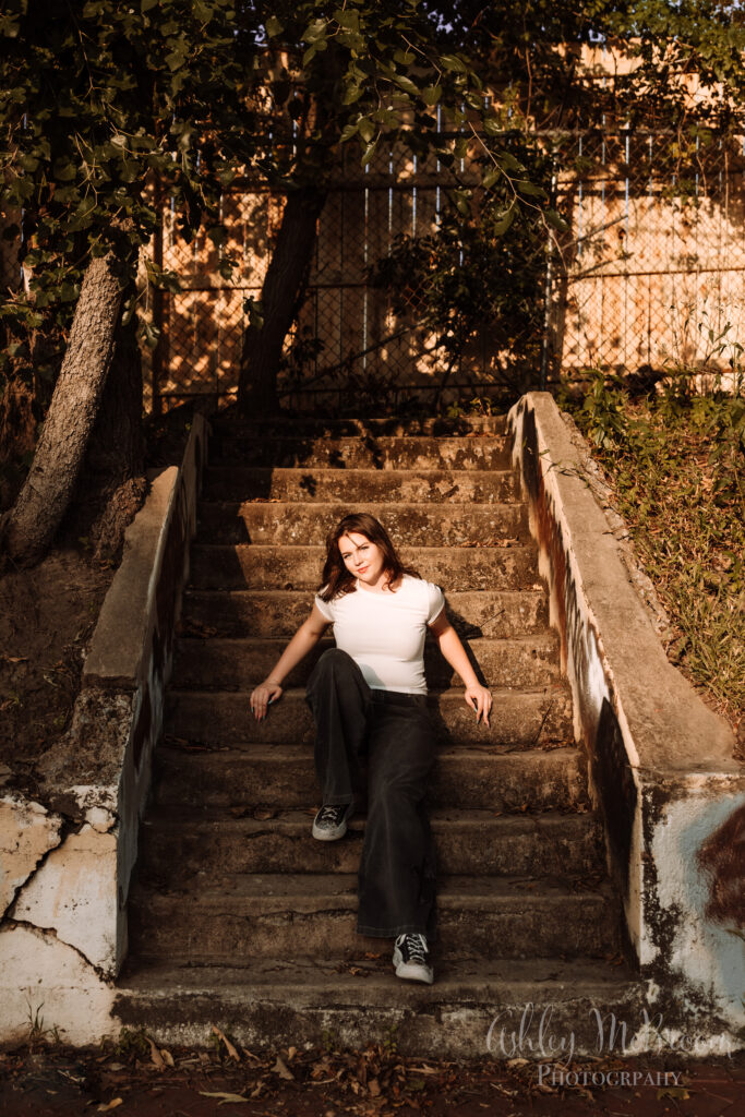girl in urban location sitting in creative light on stairs for senior pictures