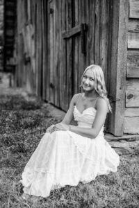 Black and white senior portrait seated by a barn of a Pope High School senior during her outdoor session