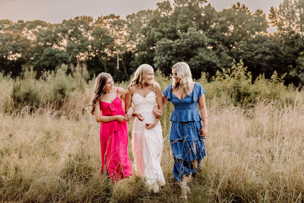Three high school senior friends walking together through a field at golden hour