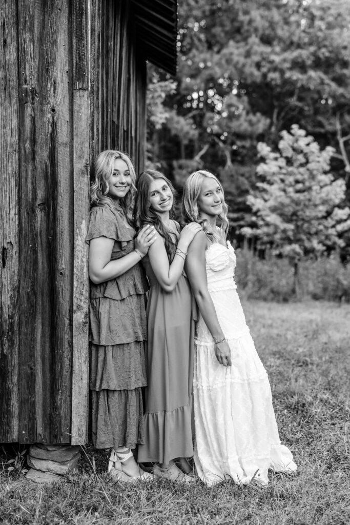 Black and white senior pictures with friends beside a rustic wooden barn in Marietta