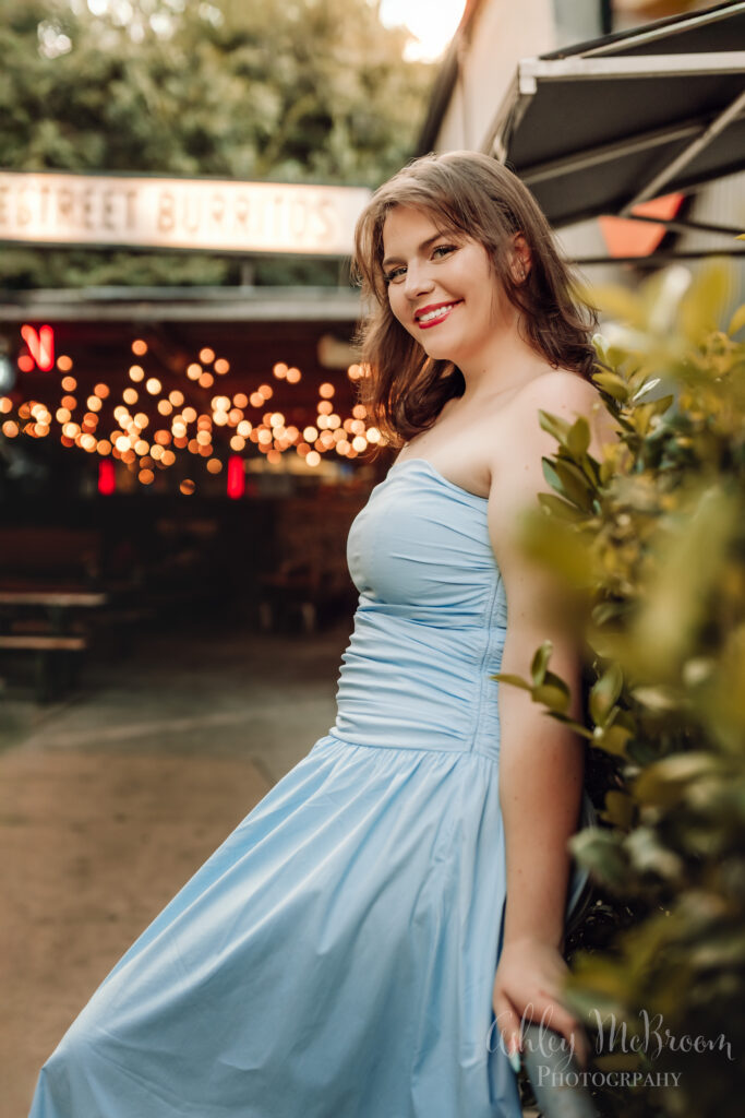 beautiful senior girl in blue dress outside burrito spot with twinkling lights