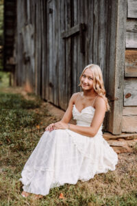 Pope High School senior in a white dress seated beside a rustic barn in Marietta, Georgia