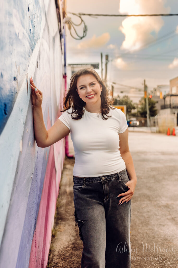 girl with sunset behind her against pastel rainbow wall during senior pictures