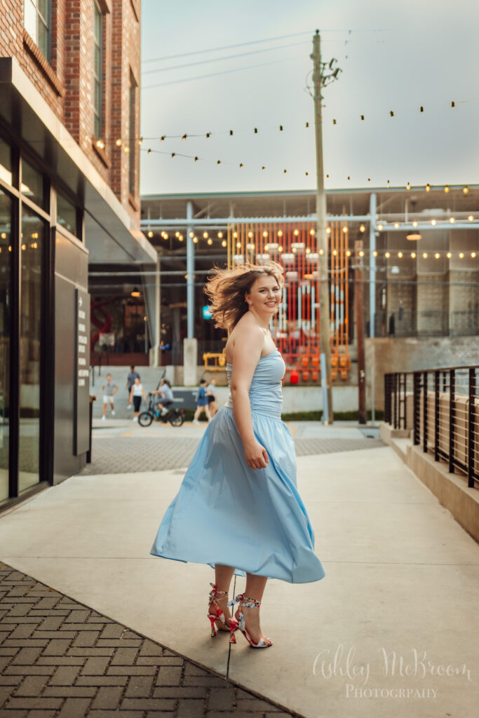 senior in beautiful blue dress twirling during urban photo shoot